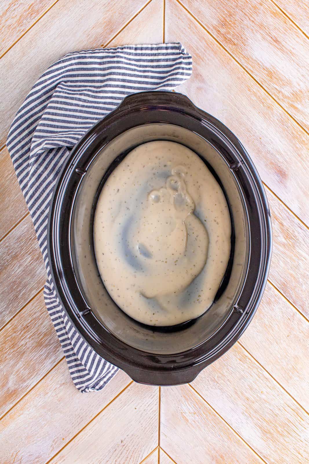 Alfredo sauce spread evenly into the bottom of an oval slow cooker.