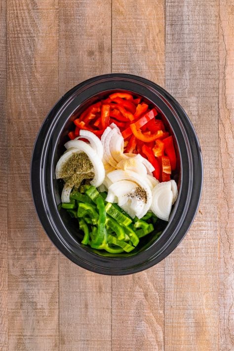Sliced onions, peppers and seasonings in a crock pot.
