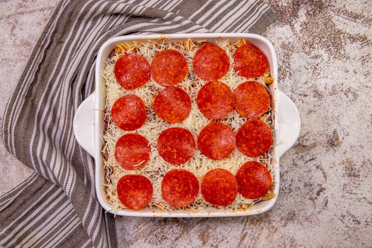 pepperoni slices placed in even layers on top of shredded mozzarella in dish. 