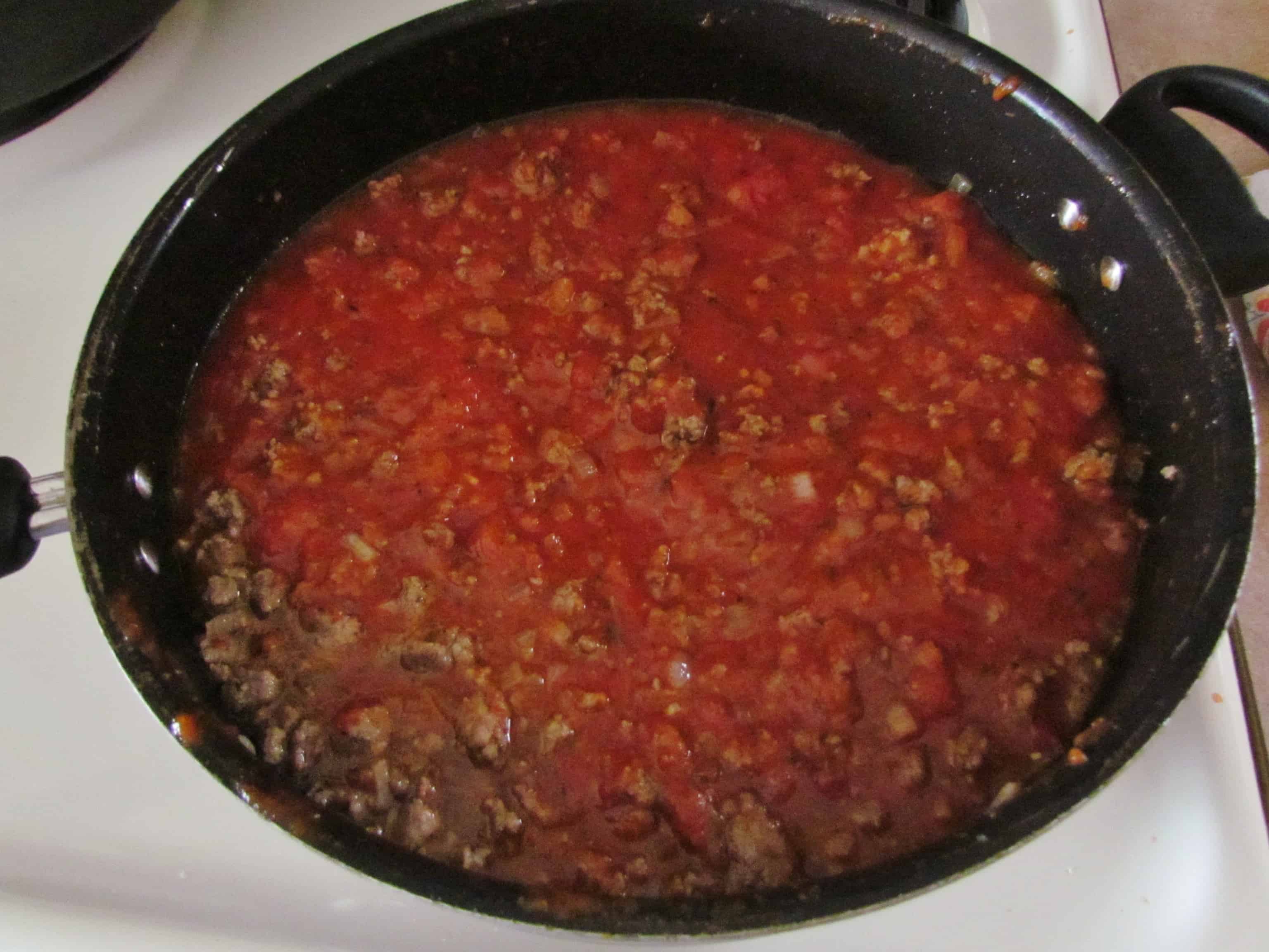 spaghetti sauce and water added to cooked ground beef in a large pan.