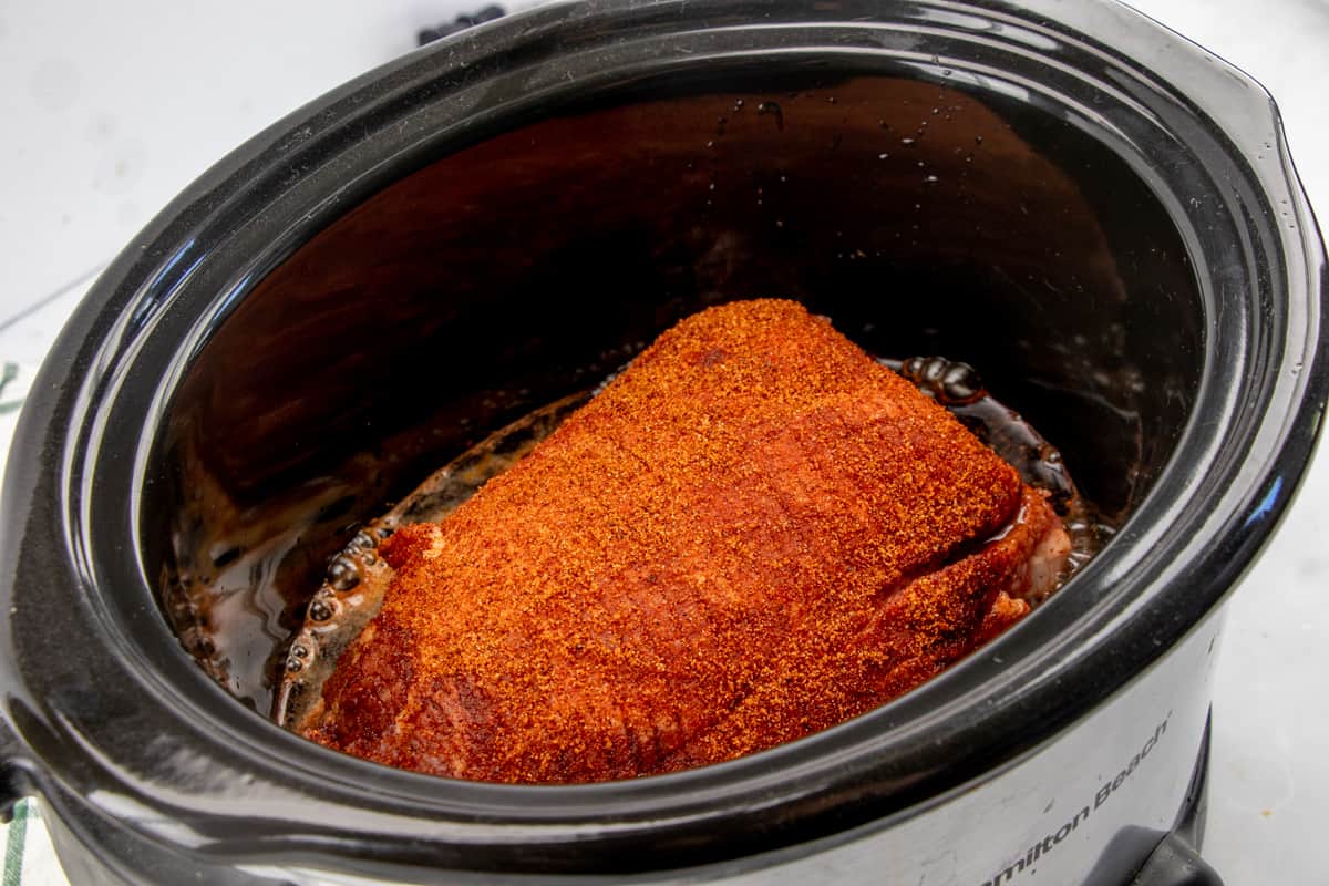 soda and liquid smoke poured around sides of pork shoulder roast in a crock pot.