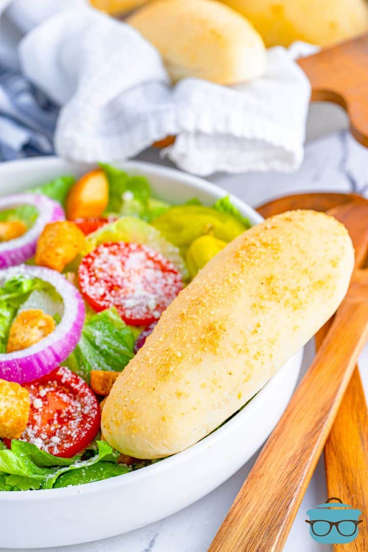 a breadstick on the side of a white bowl holding a salad. 