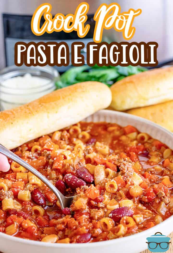 Crock Pot Pasta e Fagioli shown in a white bowl with a spoon and a piece of garlic bread on the side. 