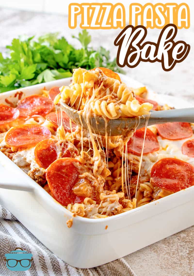 Pizza pasta fully cooked in a white casserole dish with a spoon lifting up a serving out of the dish.