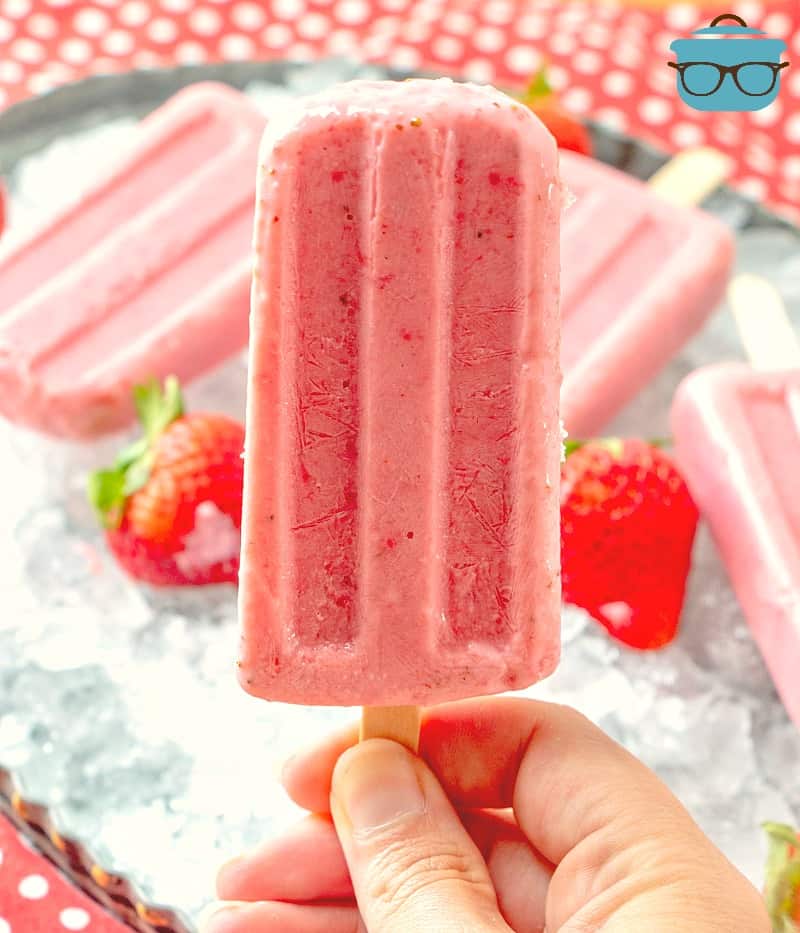 Homemade Strawberry Greek Yogurt Popsicles on a Stick being held up by a hand.