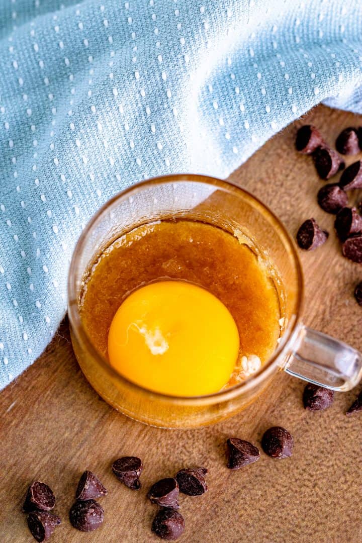 egg yolk added to melted brown sugar in a clear mug.