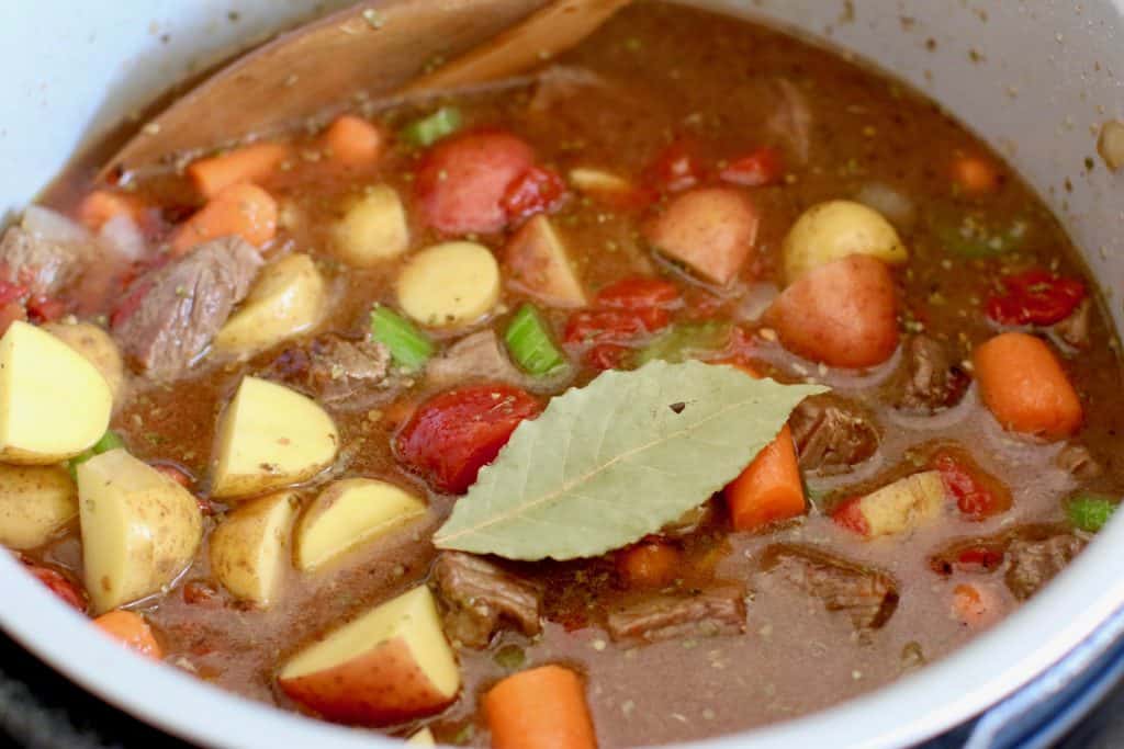 potatoes, carrots, beef broth and diced tomatoes added to Instant Pot with bay leaf on top