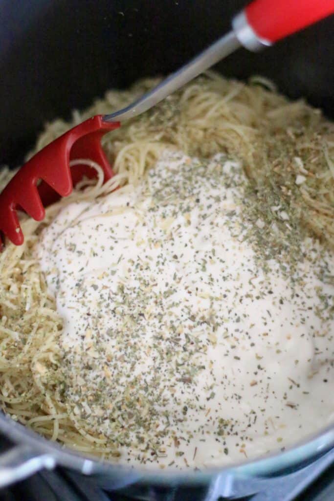 Alfredo sauce and Italian seasoning stirred together with cooked spaghetti noodles in a large stock pot