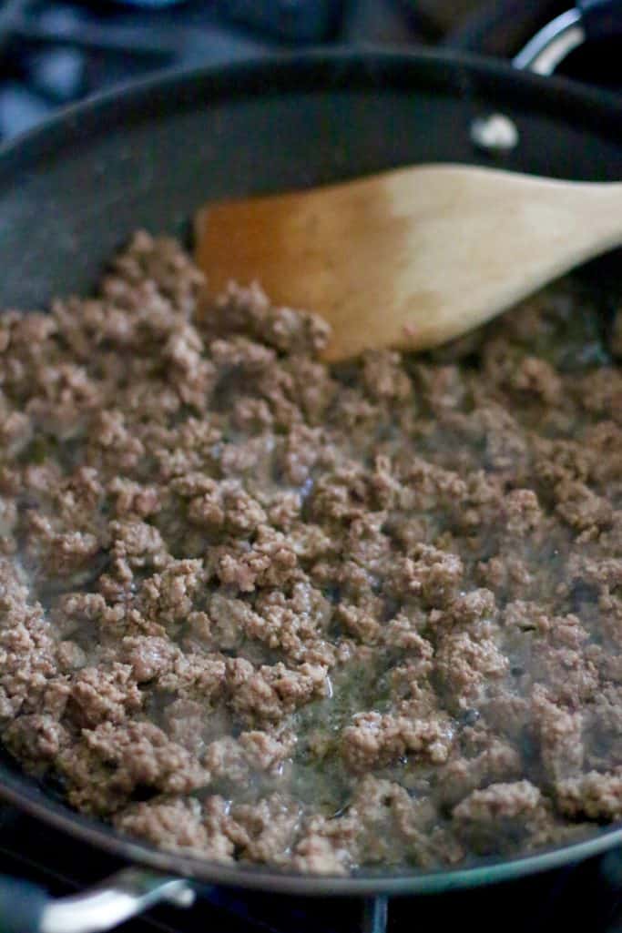 browning and crumbling ground beef in a large nonstick skillet with wooden spoon