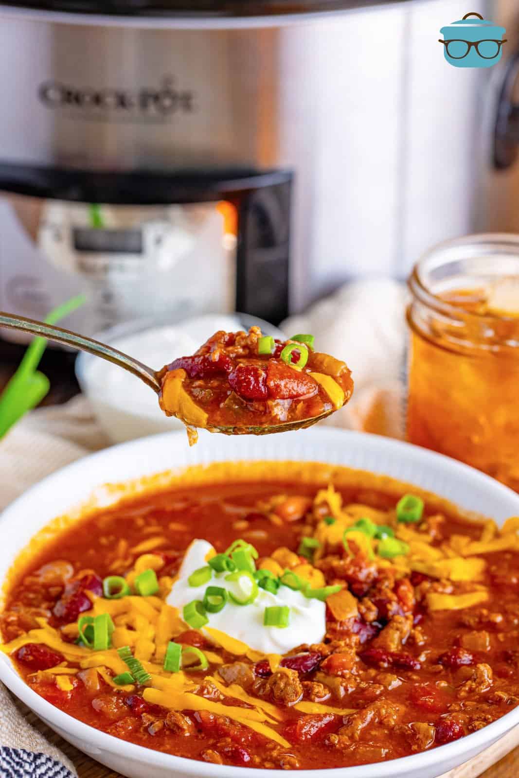 a spoon holding up some chili over a bowl. 