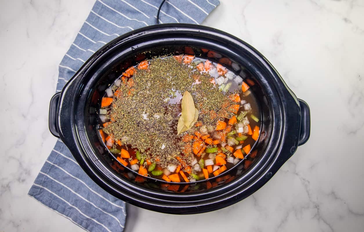 chicken, celery, onions, carrots, seasoning, chicken stock, fire roasted diced tomatoes and bay leaves added into the bottom of an oval slow cooker.