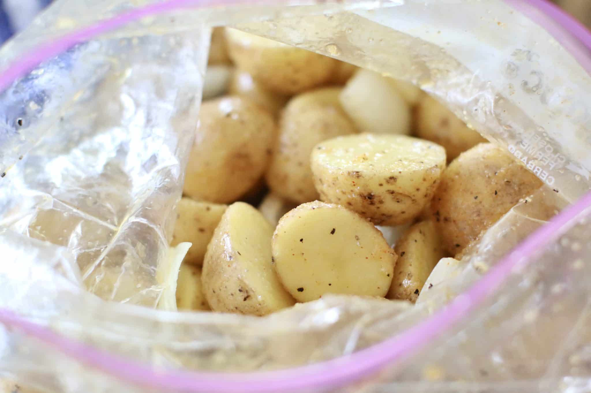 oil coated potatoes and onions in a plastic zip top bag