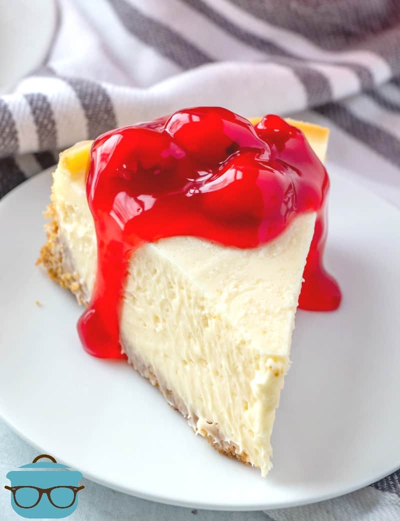 Instant Pot Cheesecake, slice on a white plate topped with cherry pie filling.