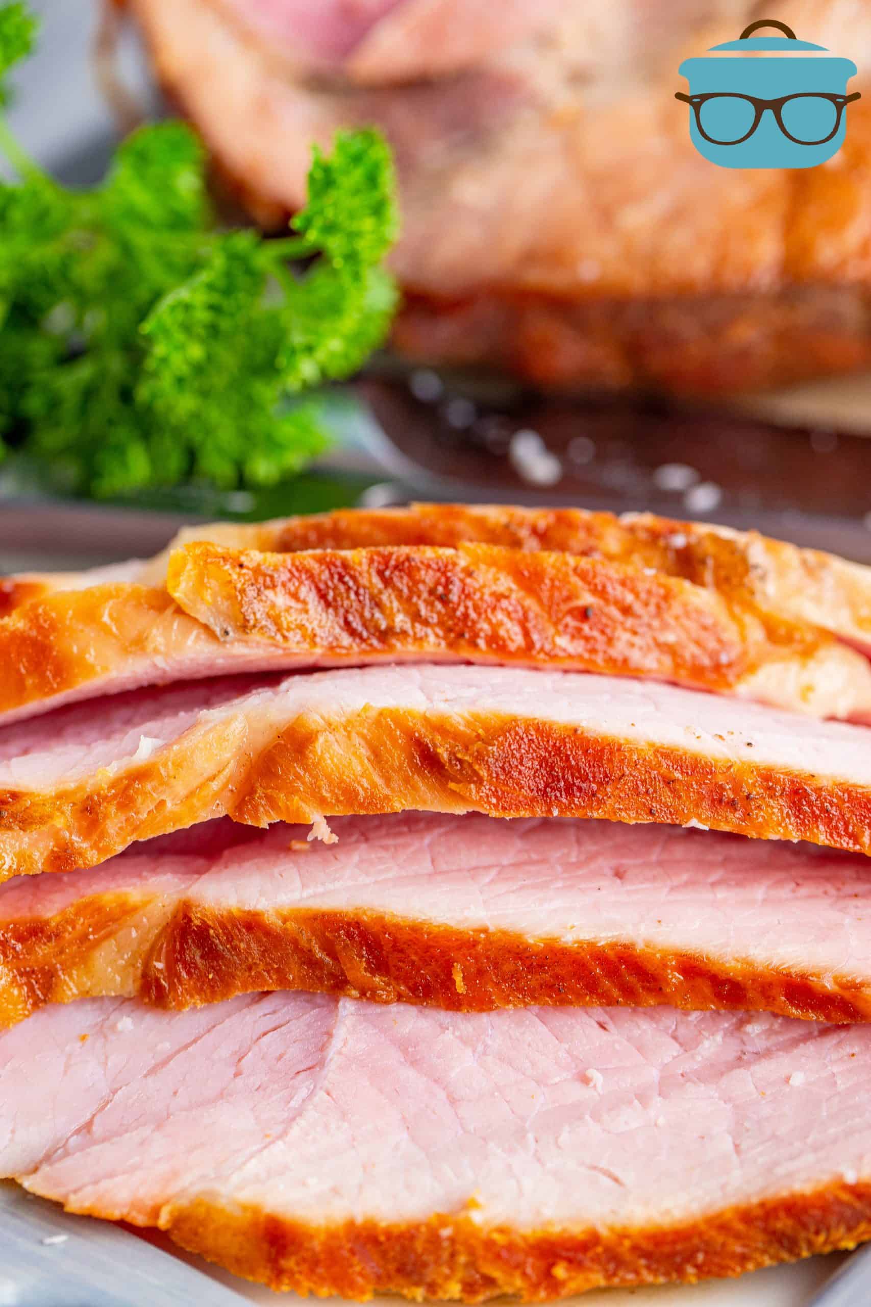 close up photo of four thinly sliced pieces of cooked ham on a white plate with fresh parsley in the background.