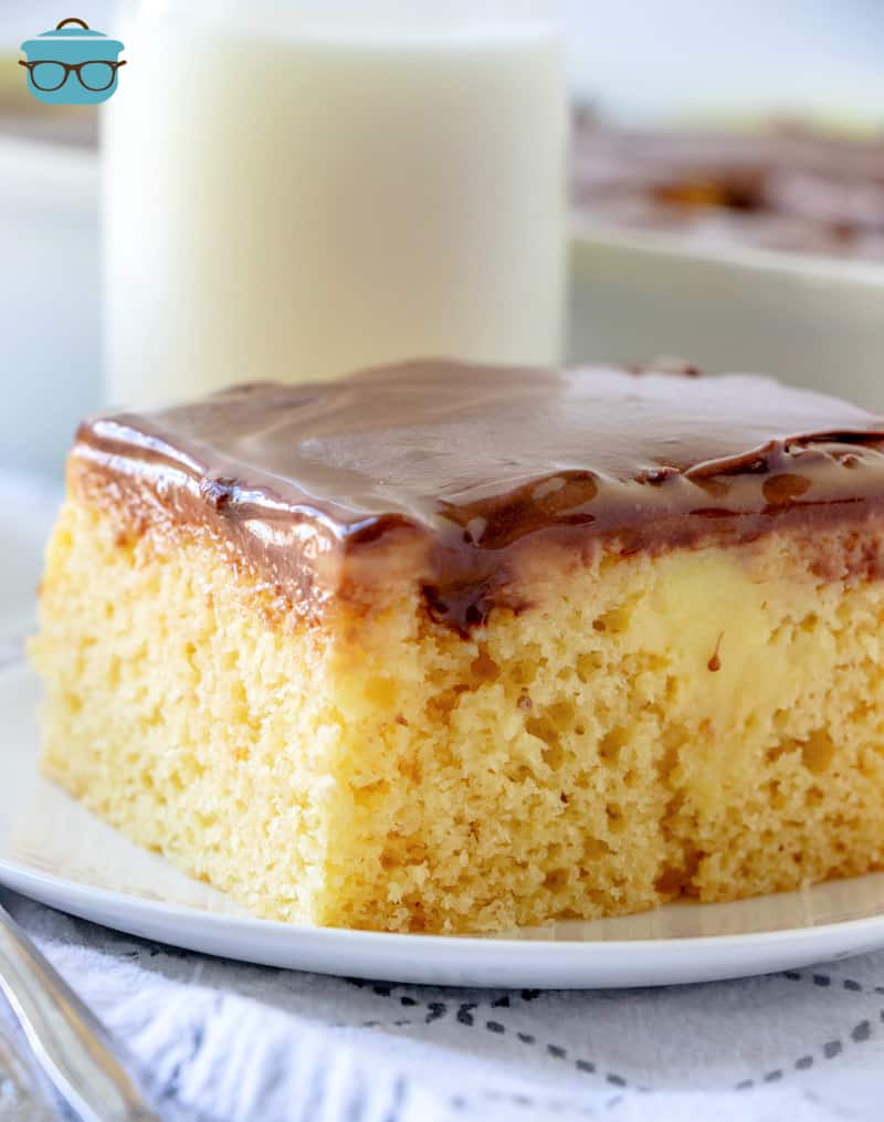 slice of Boston cream poke cake on a white plate with a glass of milk in the background. 