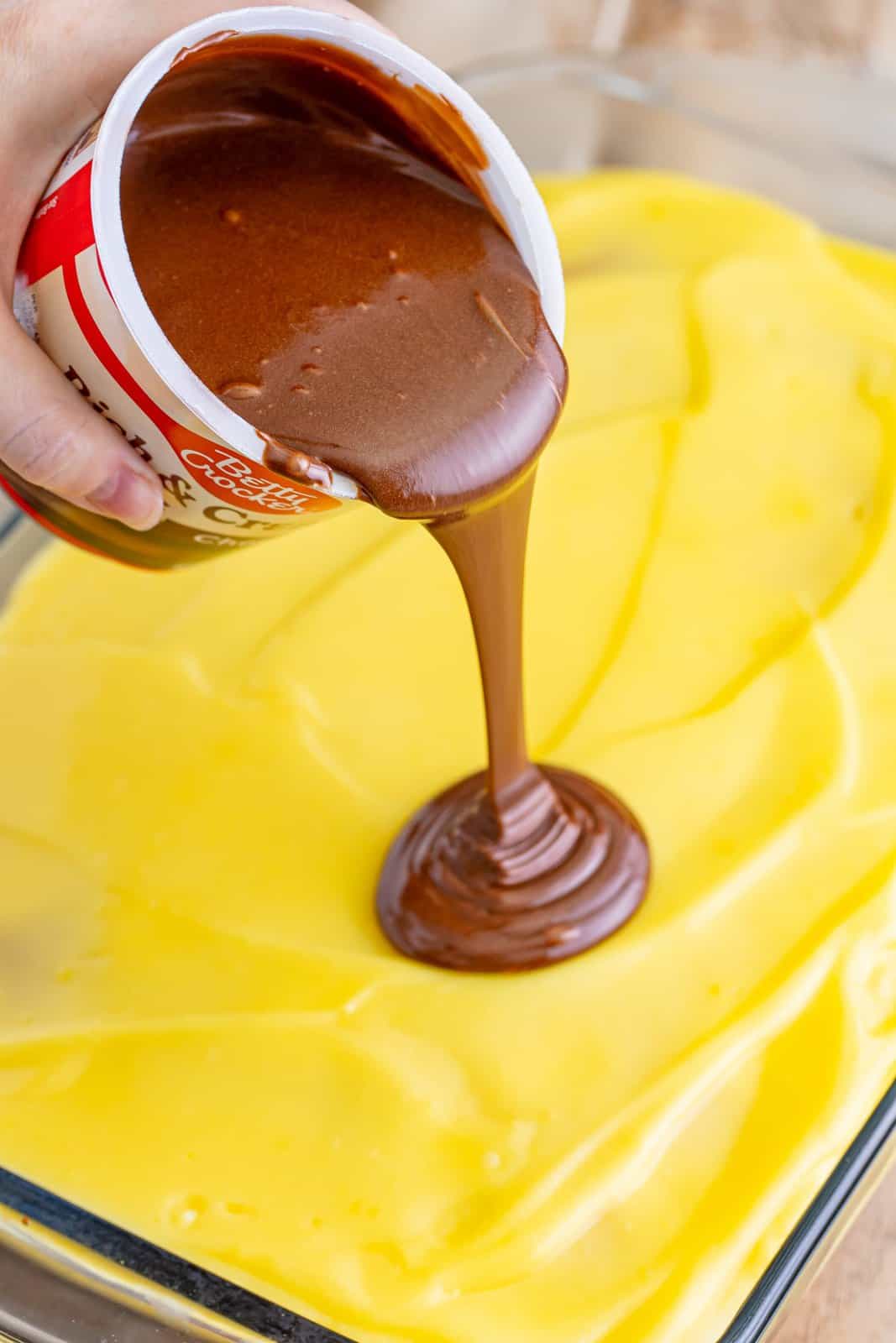 pouring chocolate frosting on top of vanilla pudding on top of cake. 