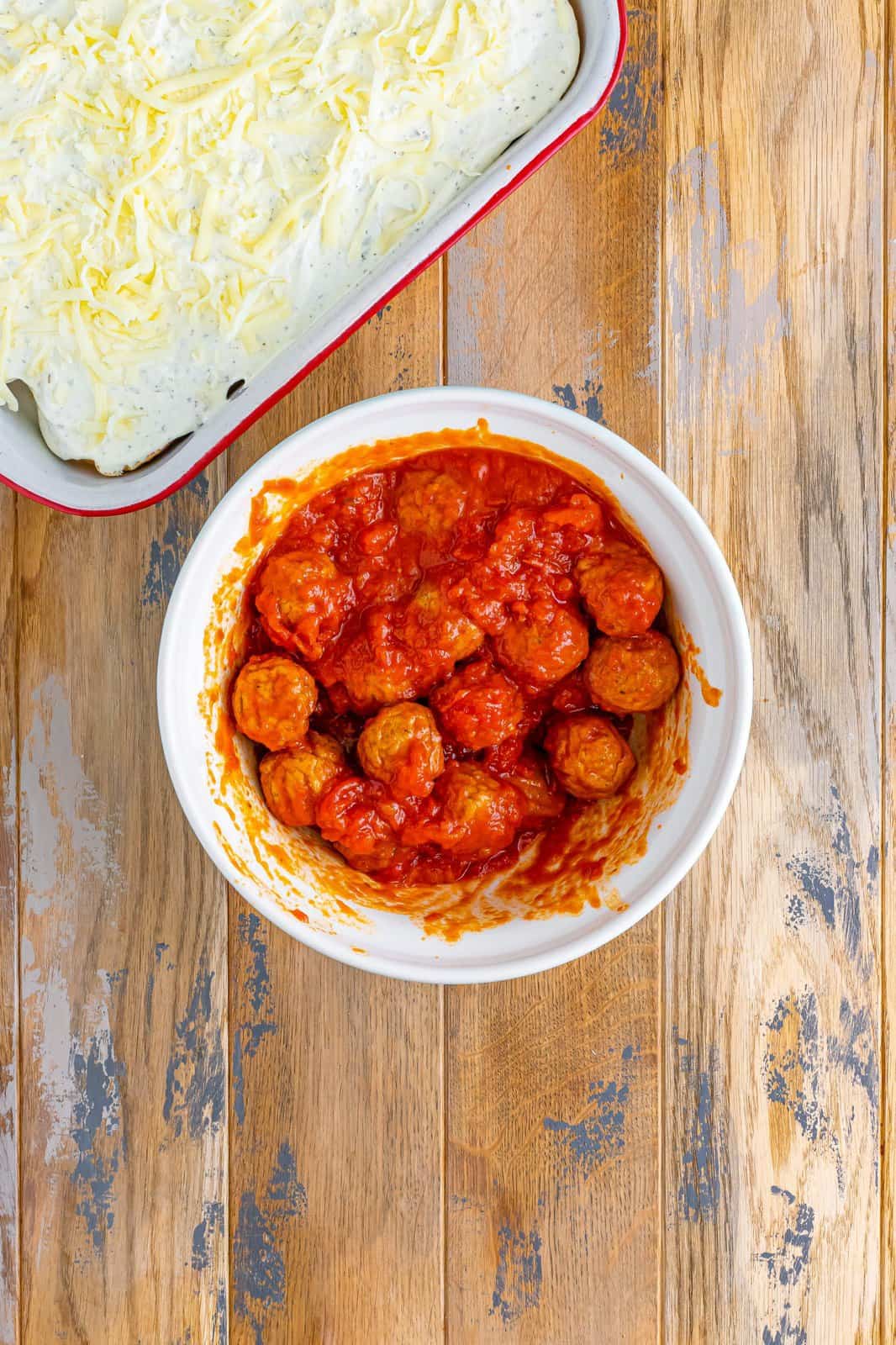 thawed Italian style meatballs shown mixed together with pasta sauce in a white bowl. 