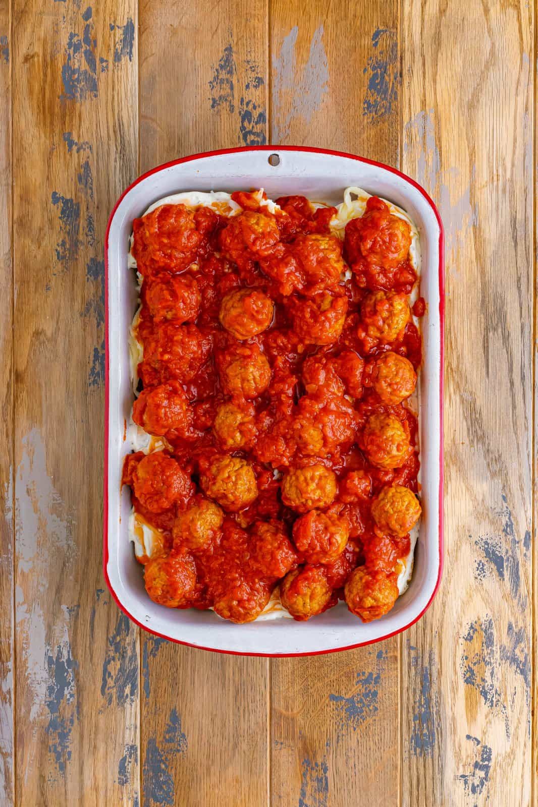 pasta sauce and meatballs shown spread out on top of casserole dish. 