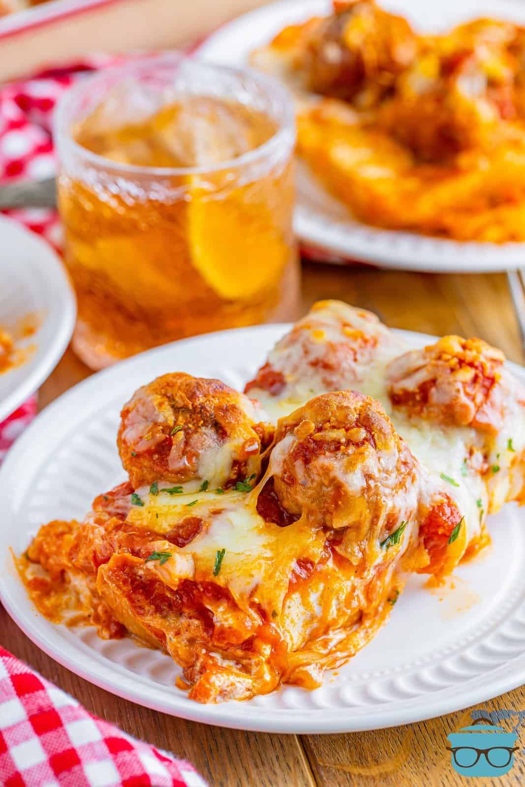 a slice of meatball sub casserole shown on a white plate with a glass of iced tea in the background.