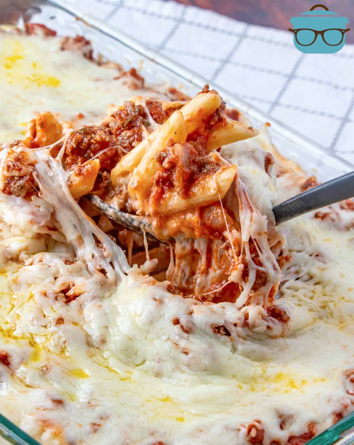 baked penne pasta topped with melted cheese scooped up with a large spoon