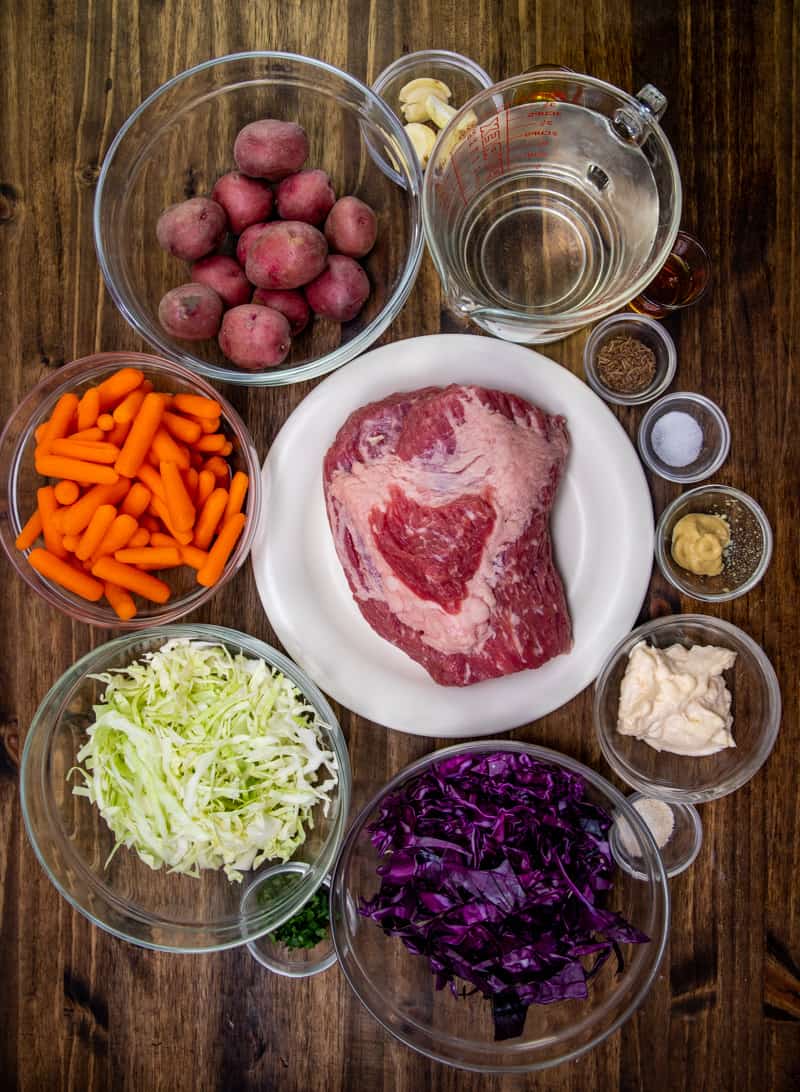 corned beef brisket, whole garlic cloves, water, baby red potatoes, baby carrots, olive oil, garlic salt, mayonnaise, honey, light olive oil, Dijon mustard, caraway seeds, red cabbage, green cabbage, parsley.