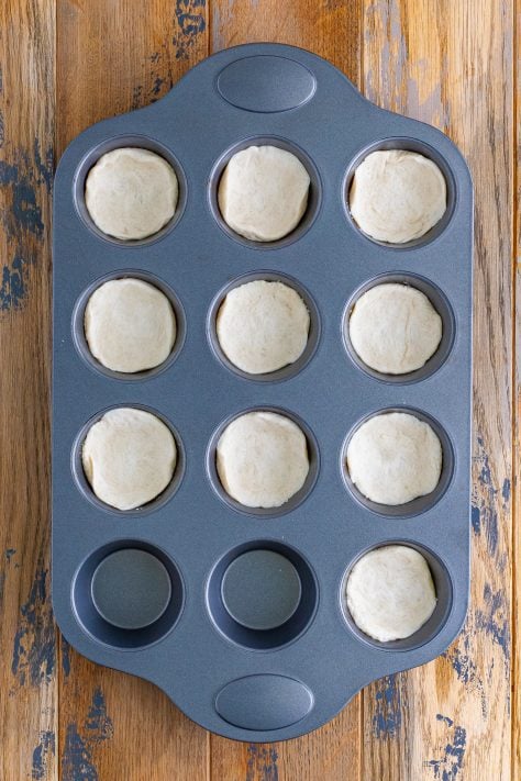 A muffin pan with pieces of biscuit dough in each well.
