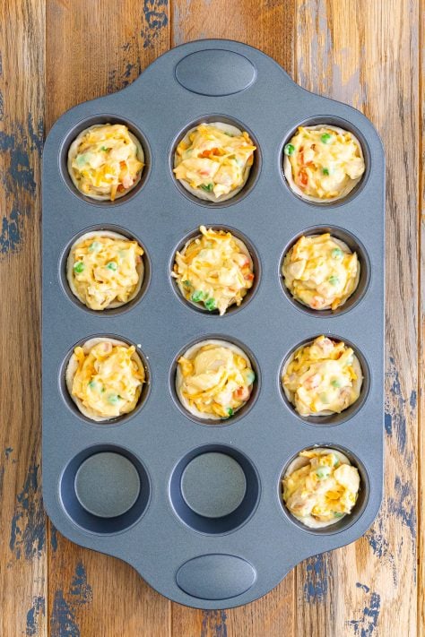 A muffin pan with unbaked Mini Chicken Pot Pies with shredded cheese on top.