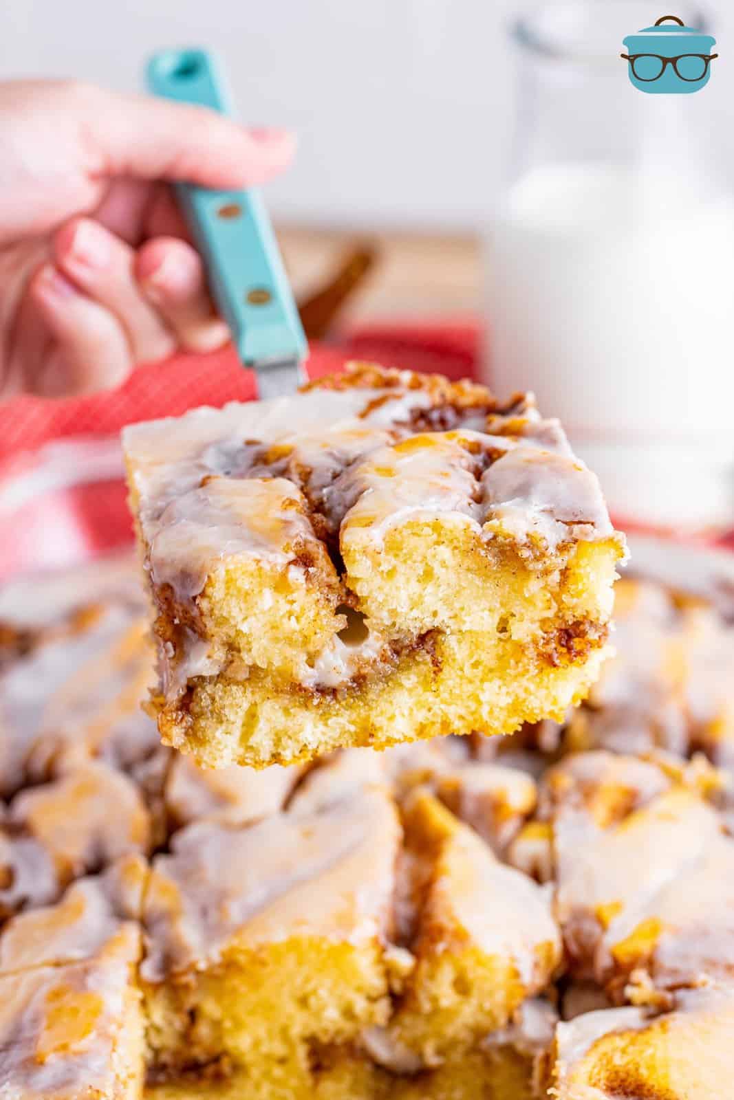 a spatula holding up a slice of cinnamon roll cake over the baked cake in a baking dish. 