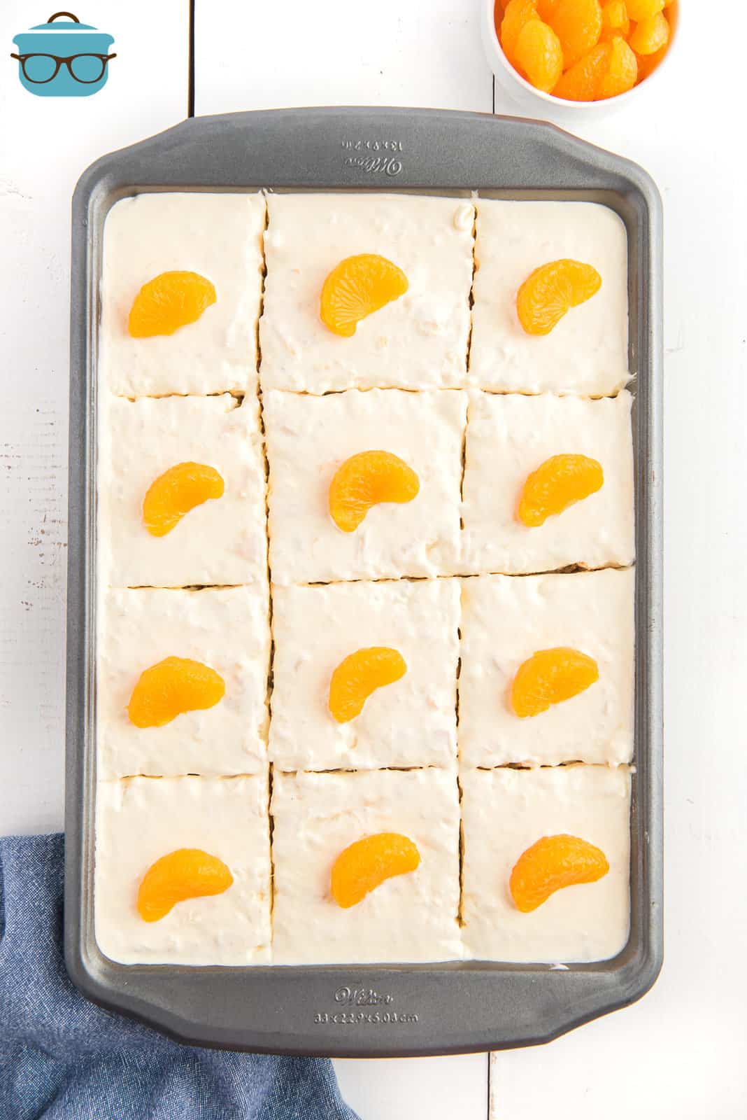 sliced pig picking cake in the baking dish cut into 12 slices and each slice topped with a mandarin orange. 