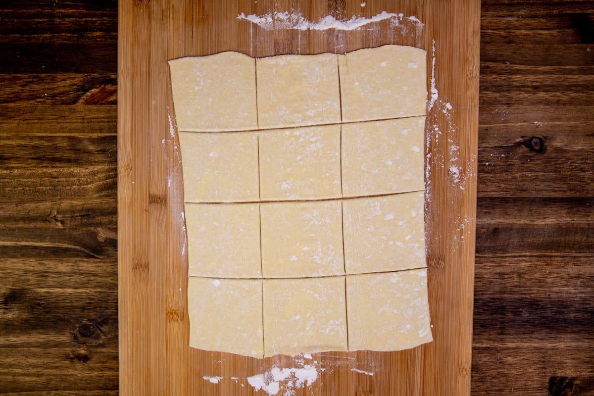 puff pastry cut into 12 squares on a cutting board.