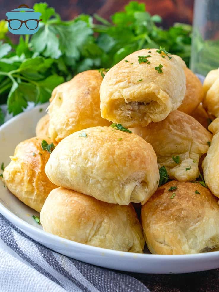 Sausage Rolls stacked on a plate with parsley in the background.