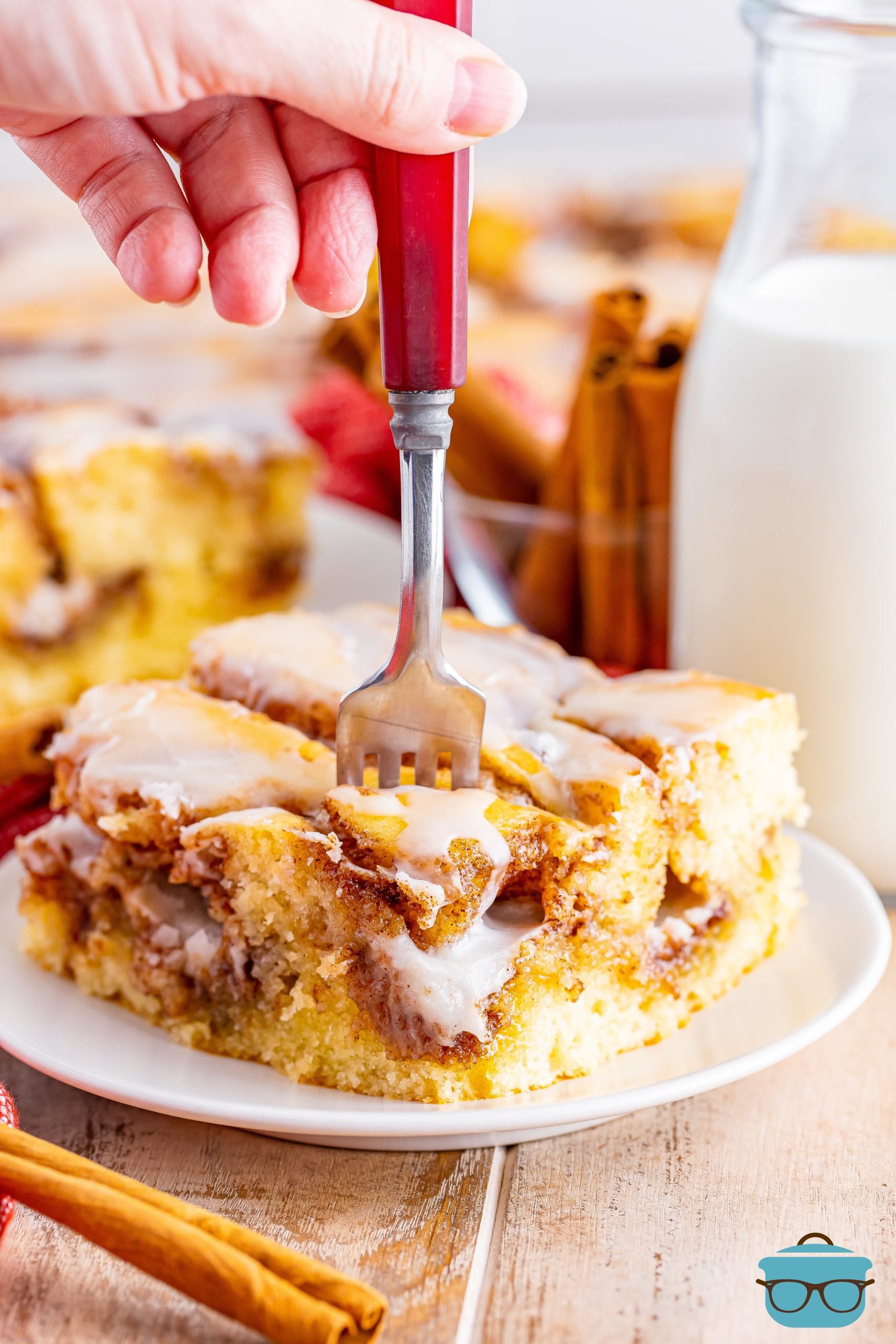 a fork being inserted into a slice of cinnamon rolls cake on a white plate. 