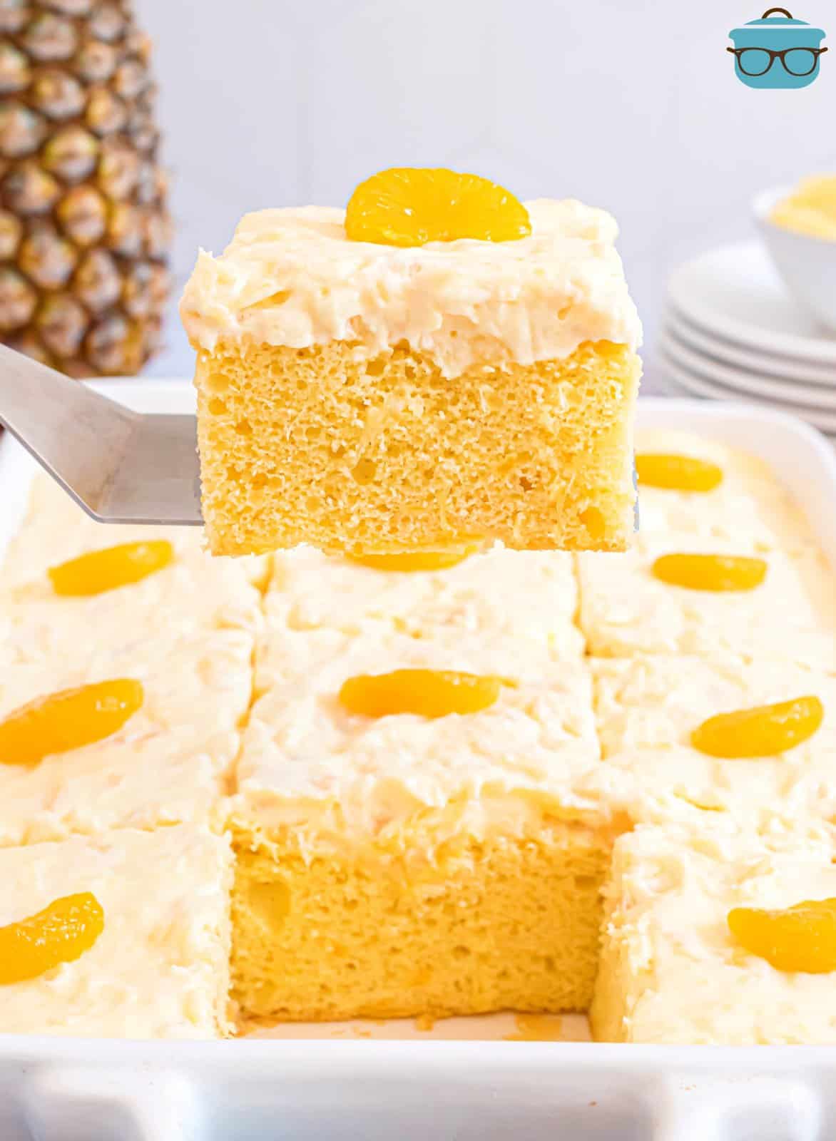 a slice of mandarin orange cake being held up over the baking dish with a metal spatula.