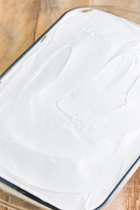 Whipped topping over a layered pudding and cake cake in a glass baking dish.