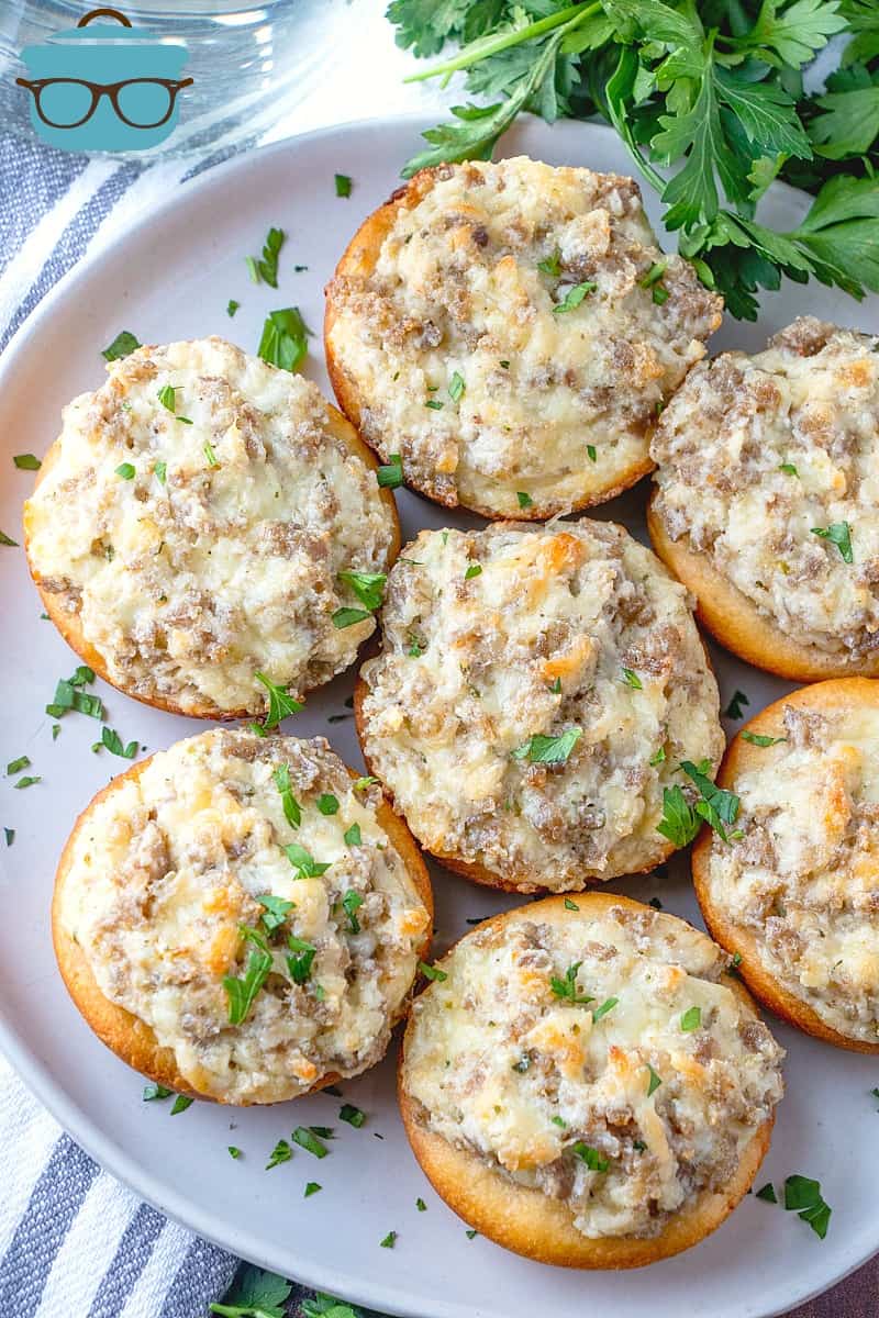 Cream Cheese Stuffed Sausage Biscuits topped with chopped fresh parsley displayed on a round white platter.