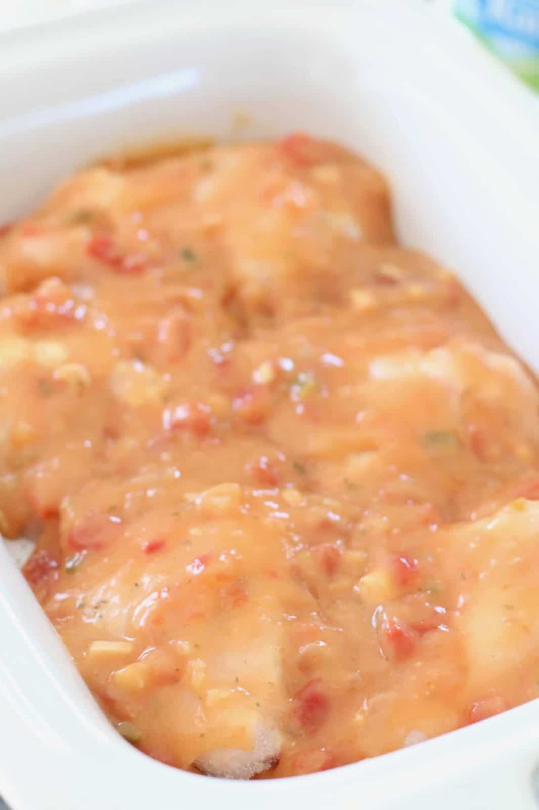 salsa mixture poured evenly over frozen chicken breasts in a white casserole crock pot.