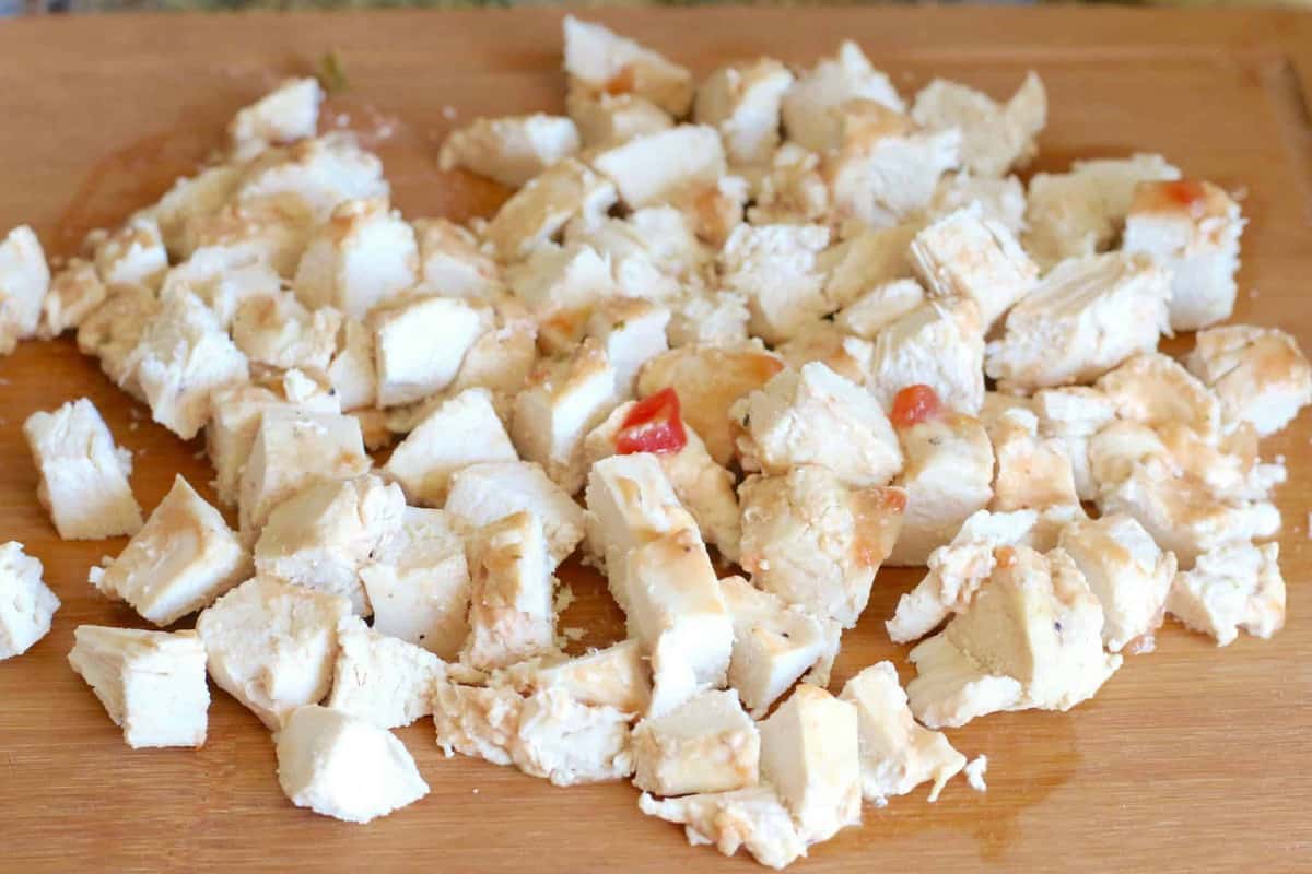 cooked chicken cut into chunks on a wooden cutting board.