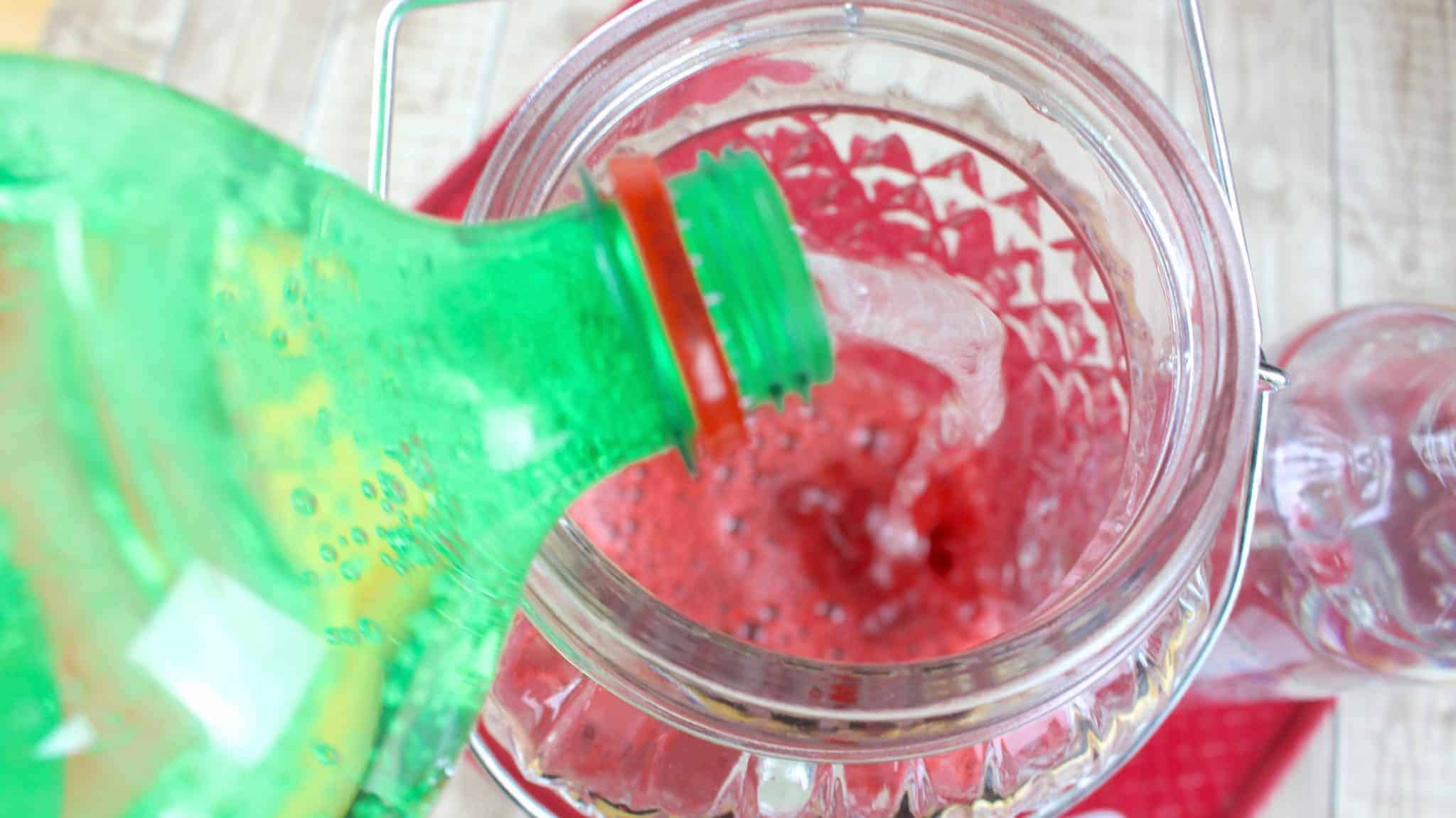 pouring 7-Up soda into the strawberry concentrate mixture in a large container.