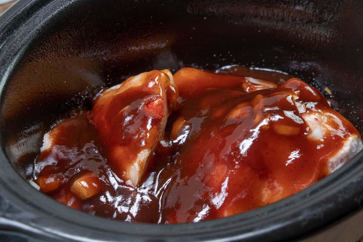 barbecue sauce poured over frozen chicken in an oval slow cooker.