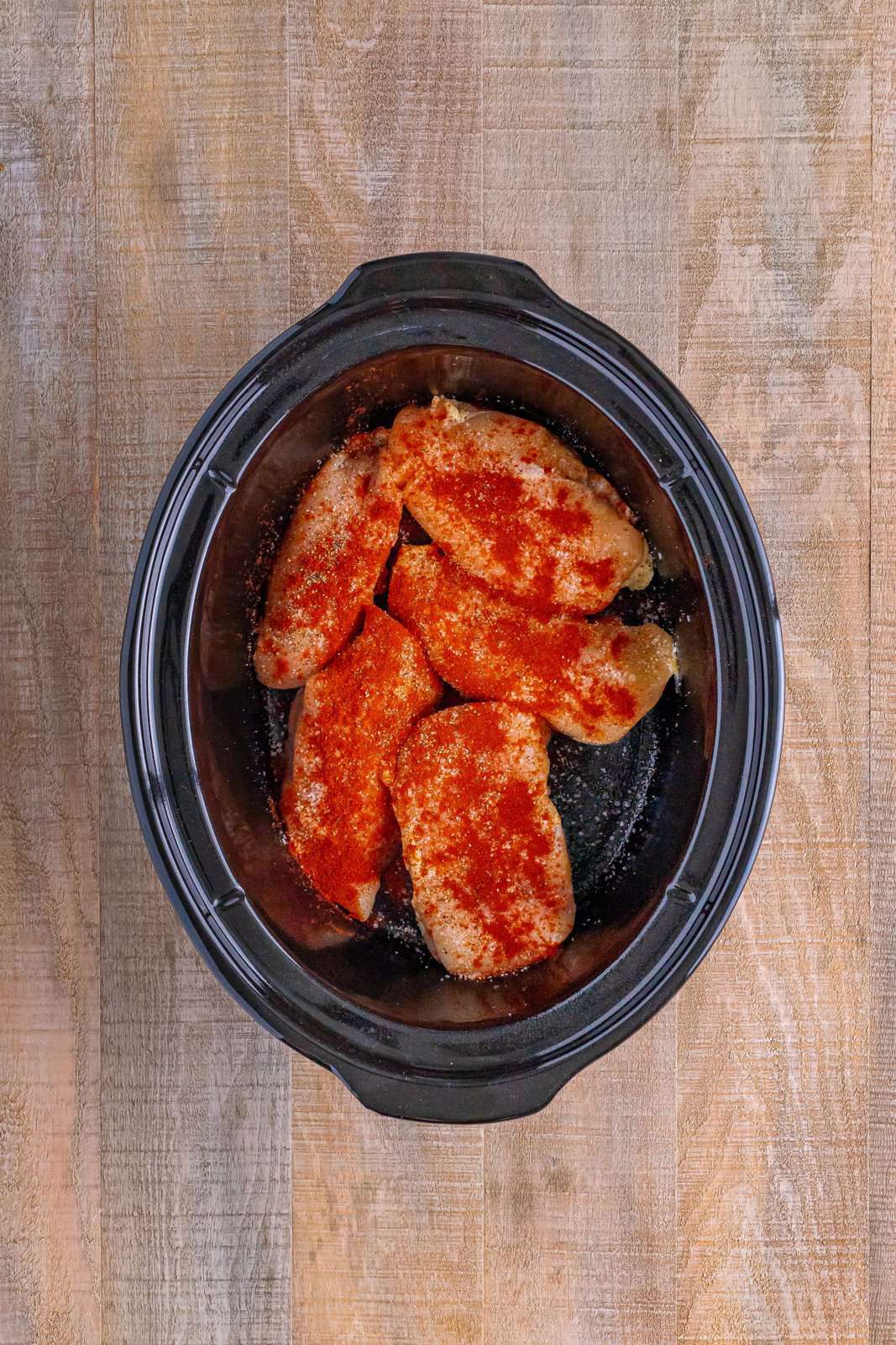 salt, pepper and smoked paprika shown on top of chicken breasts in a crock pot. 