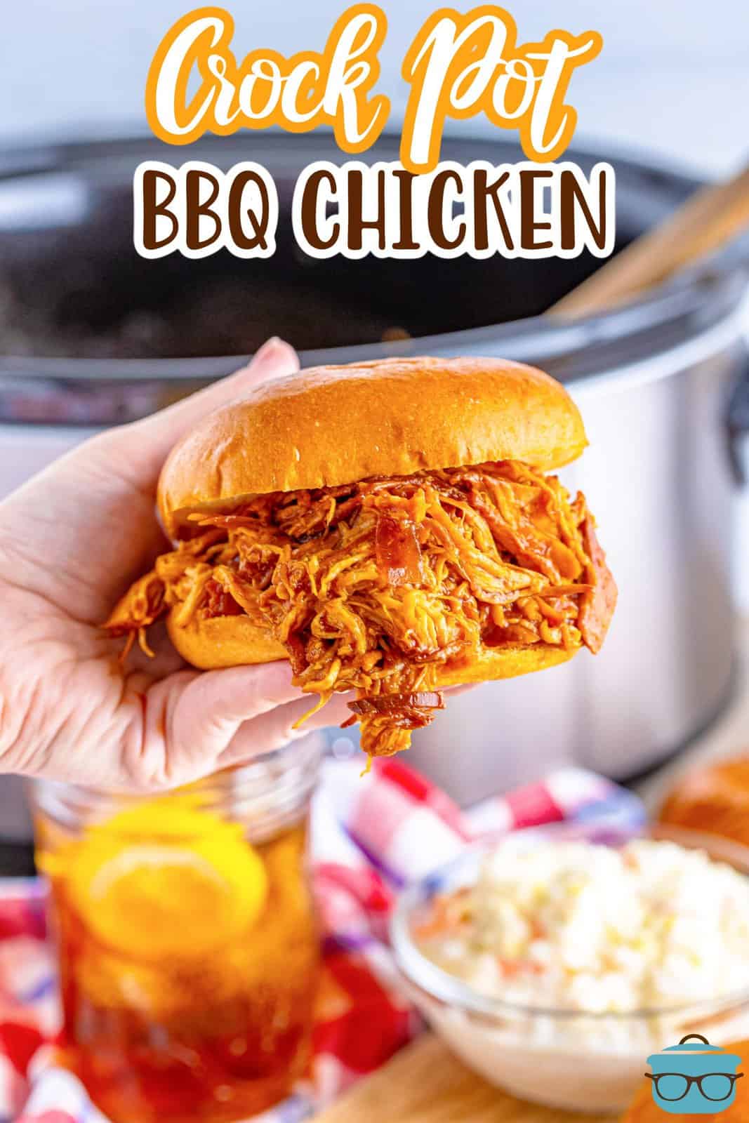 a hand holding up a shredded BBQ chicken sandwich in from of a slow cooker. 