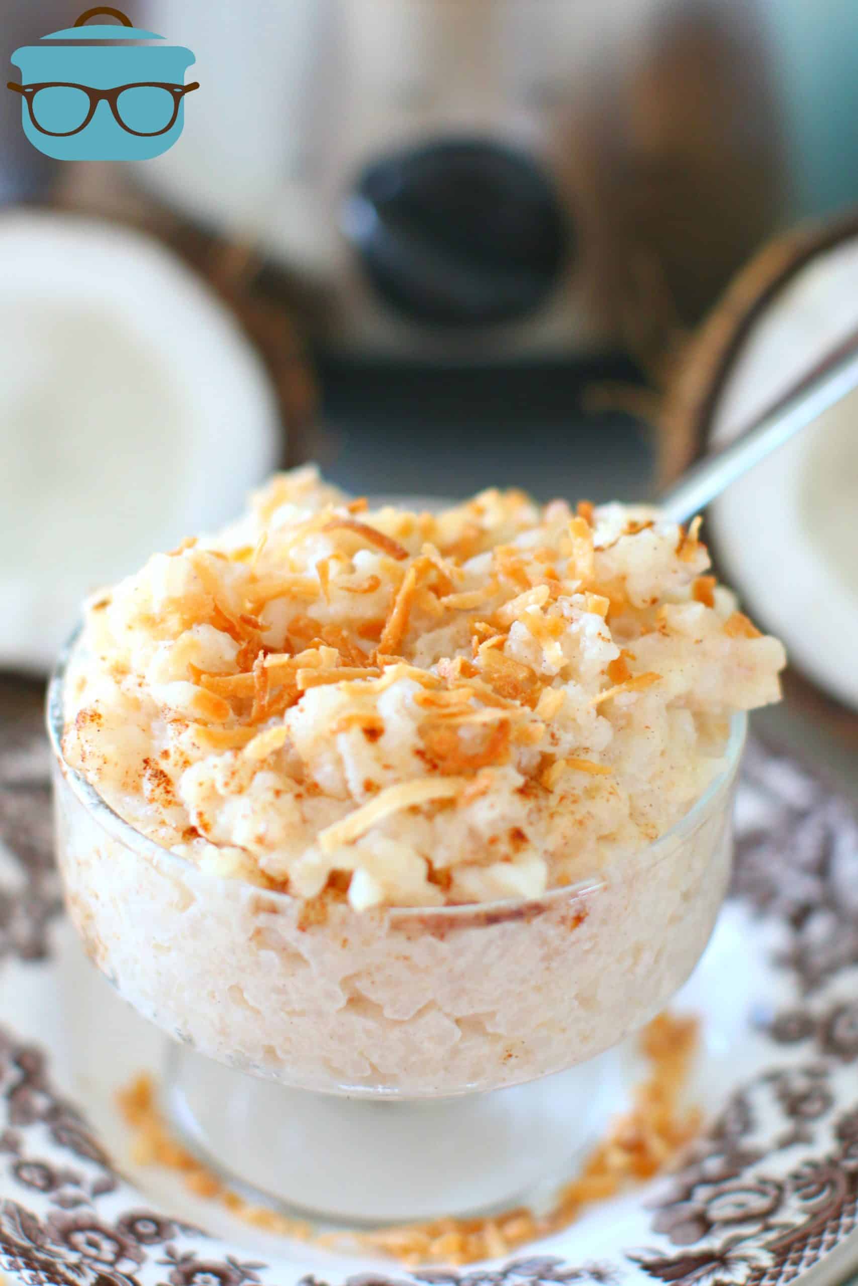 Crock Pot Coconut Rice Pudding served in a glass dessert cup on top of a plate with a chopped coconut in the background.