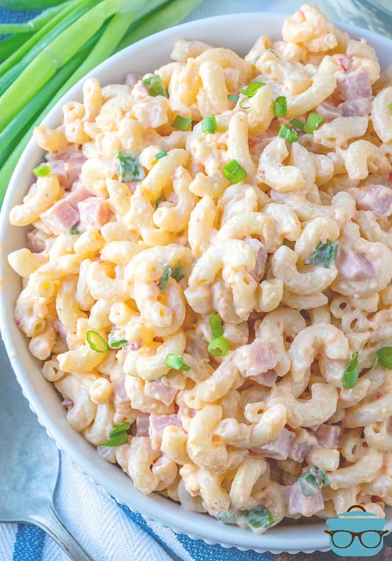 Pimiento Cheese Macaroni Salad with Ham shown served in a large white bowl with a sprig of green onions in the background.