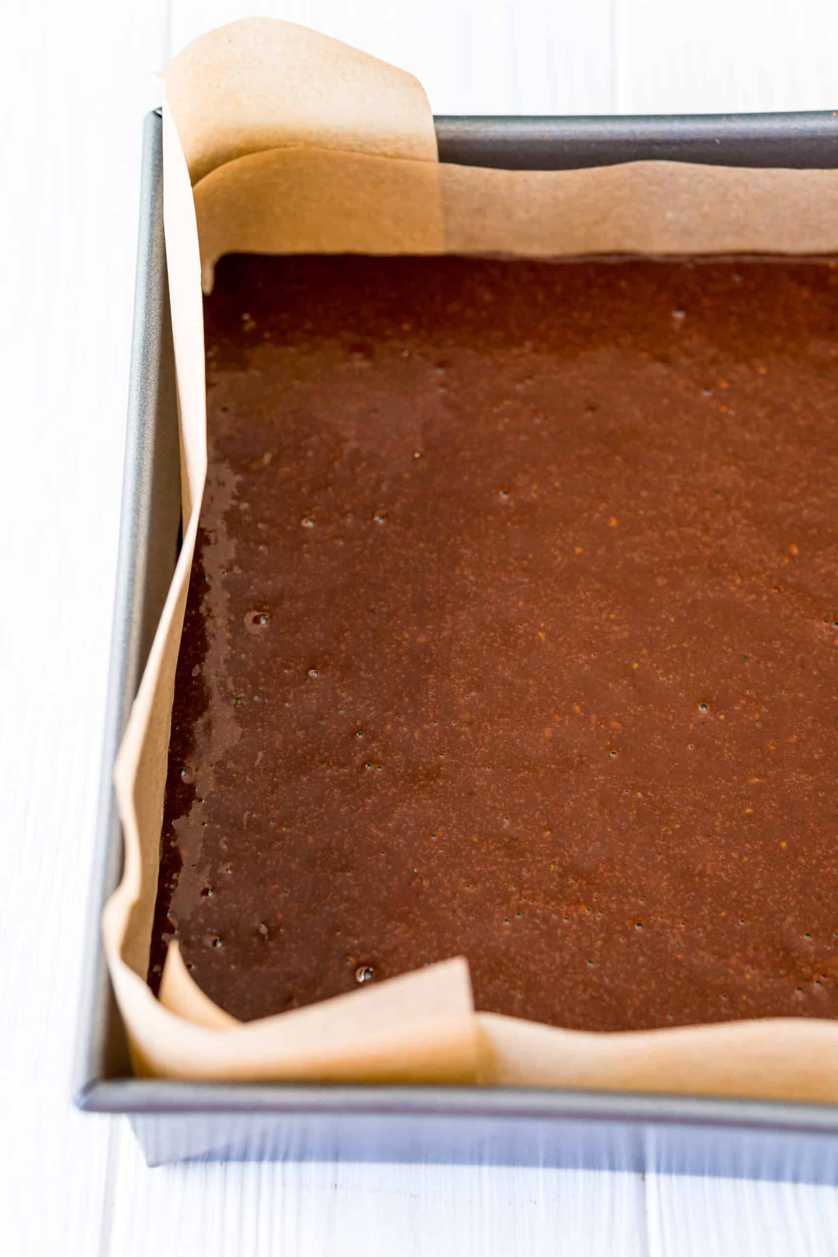 zucchini brownie batter poured into prepared baking dish with parchment paper.