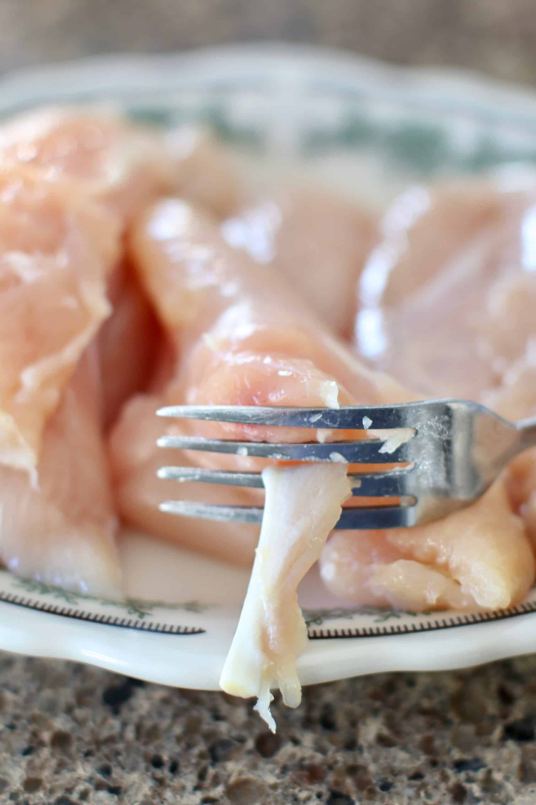 removing cartilage strip from chicken tenderloin with a fork.