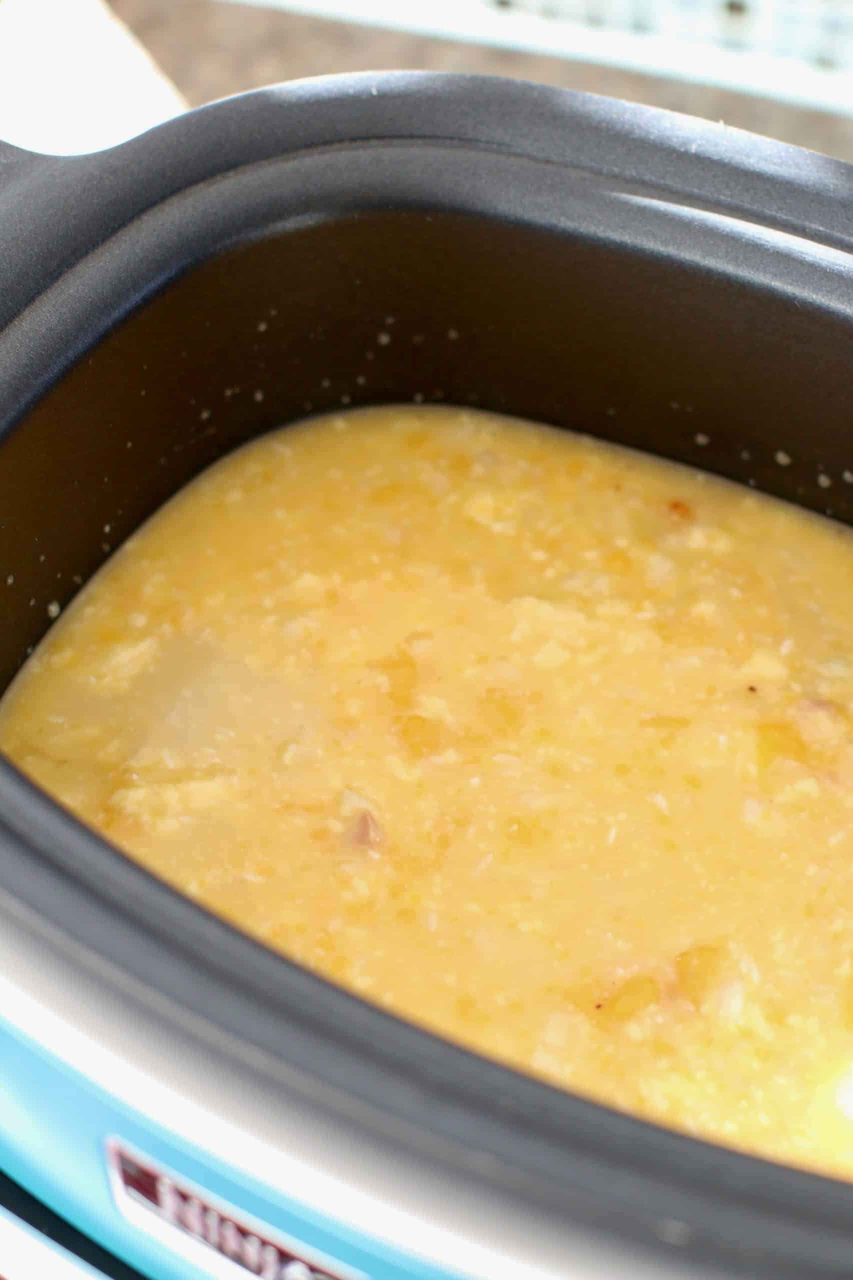 cheddar cheese soup and rice mixture poured over chicken tenders in an oval slow cooker.