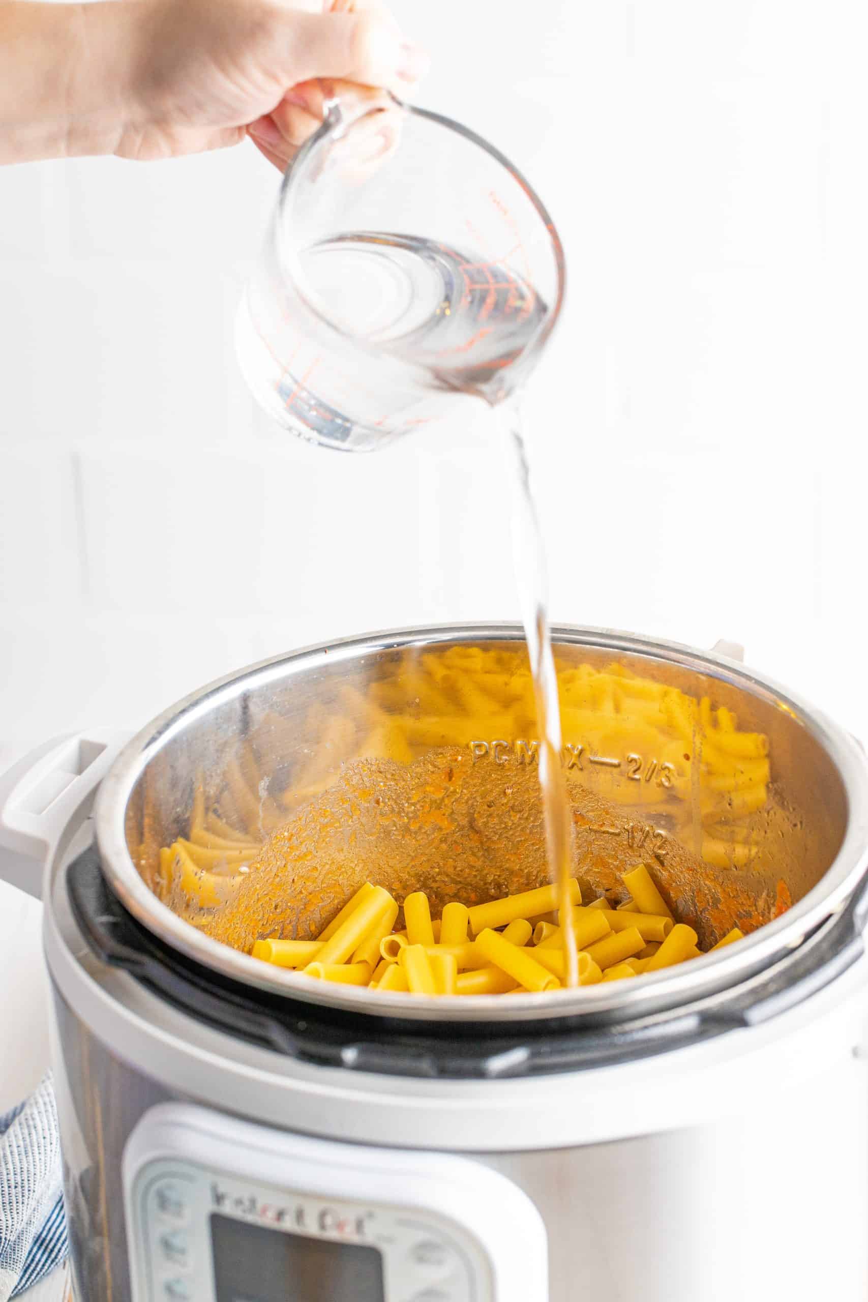 pouring water to the top of the ziti pasta noodles in an electric pressure cooker.