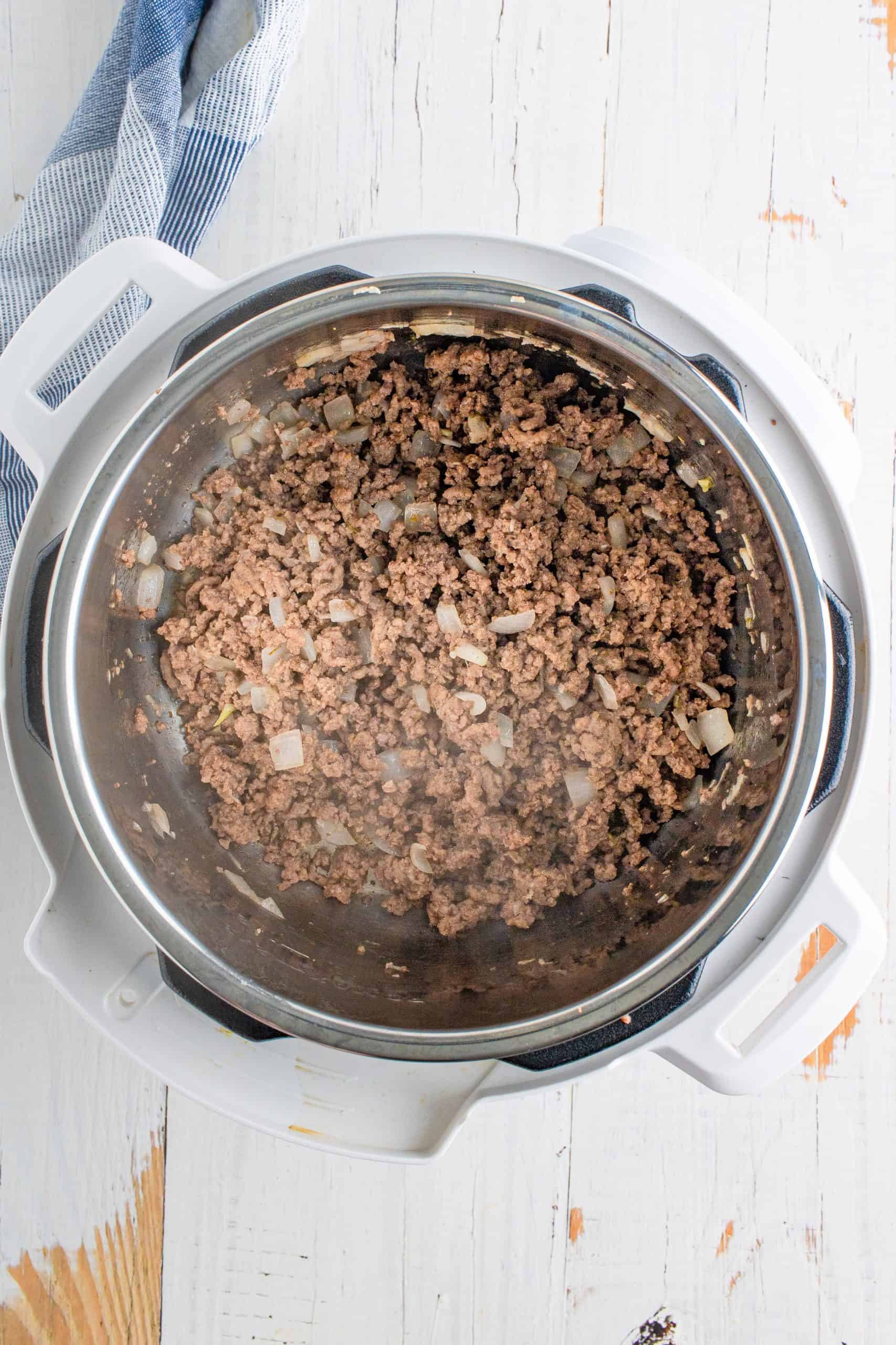 fully cooked and crumbled ground beef and cooked onion in the bottom of an instant pot.