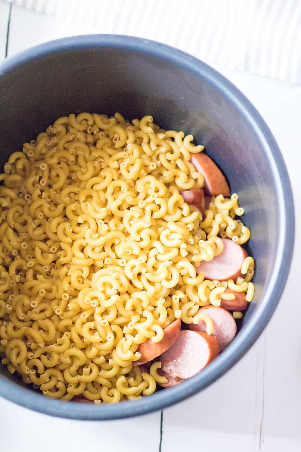 macaroni noodles and sliced sausage in the bowl of an electric pressure cooker.
