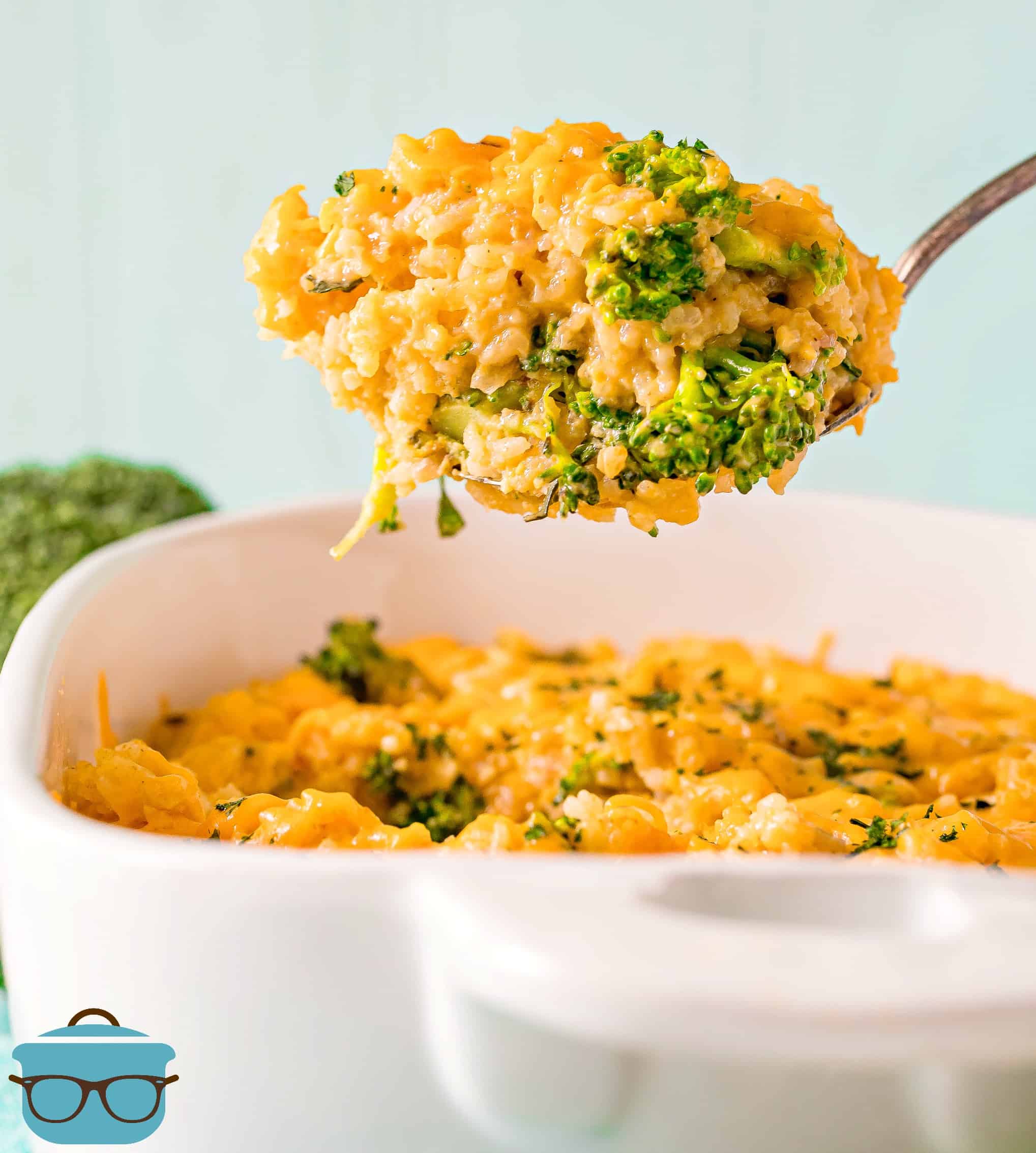large spoonful of broccoli rice cheddar casserole being held up over casserole dish.